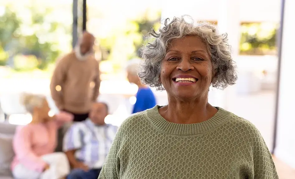 Happy elderly woman standing indoors with a group of seniors behind her